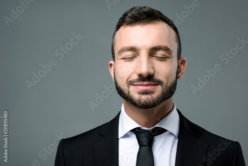 handsome smiling businessman with closed eyes isolated on grey