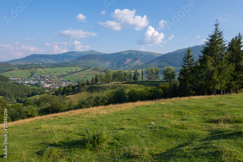 Magnificent landscape of mountain slopes and peaks standing in the distance against the background of the blue sky and lying city of the valley.