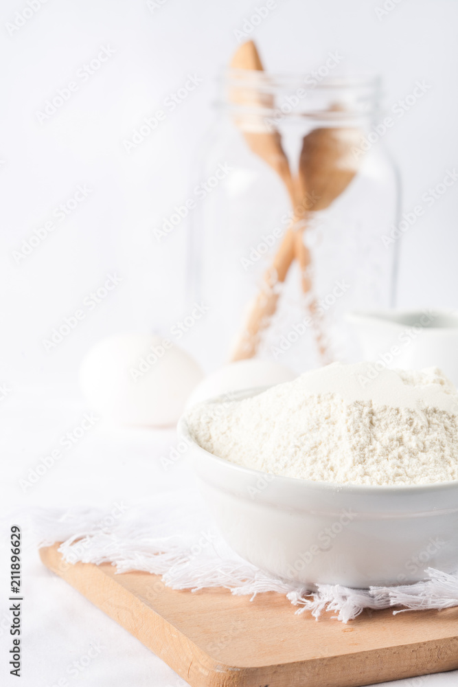 Baking ingredients. White background. Ingredients and tools to make a cake. Flour, milk, eggs, rolling pin, wooden spoons, jar. Copy space. Bakery. Baking concept Baking ingredients. White background. Ingredients and tools to make a cake. Flour, milk, eggs, rolling pin, wooden spoons, jar. Copy space. Bakery. Baking concept