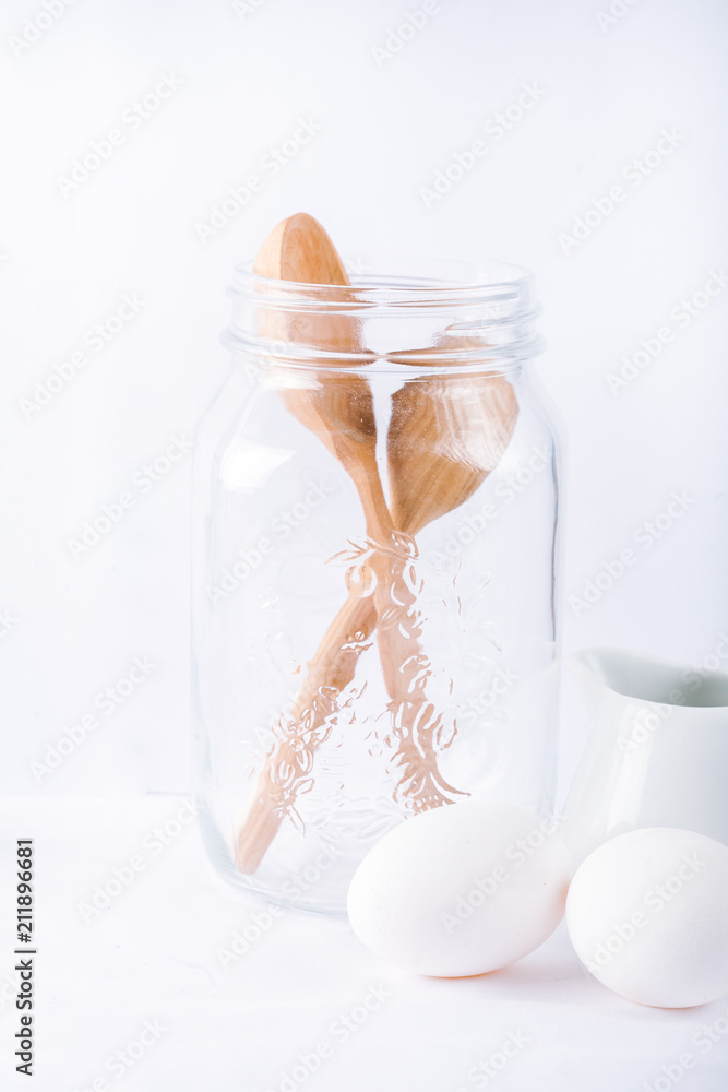 Baking ingredients. White background. Ingredients and tools to make a cake. Flour, milk, eggs, rolling pin, wooden spoons, jar. Copy space. Bakery. Baking concept Baking ingredients. White background. Ingredients and tools to make a cake. Flour, milk, eggs, rolling pin, wooden spoons, jar. Copy space. Bakery. Baking concept