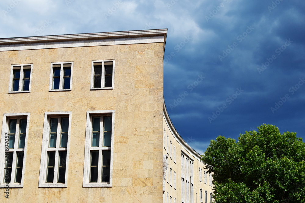 Fragment of old building with yellow facade against blue sky and green tree with copy space for text on sky in summer day in Berlin.