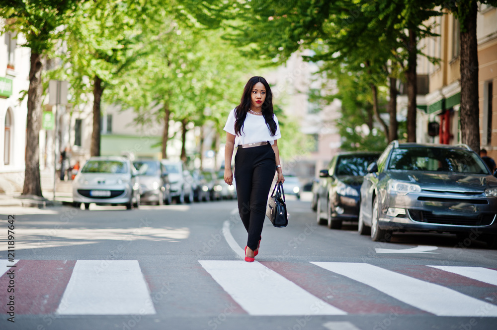 Stylish african american business woman on streets of city at pedestrian crossing.