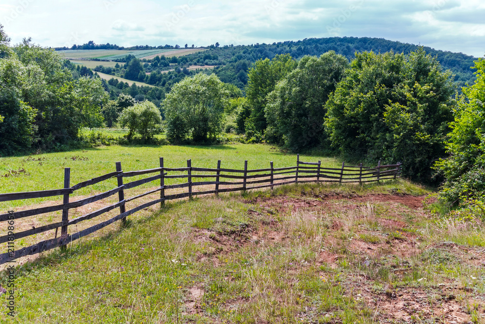 wooden fence on a hill with a blurred dirt road descending down to the bottom