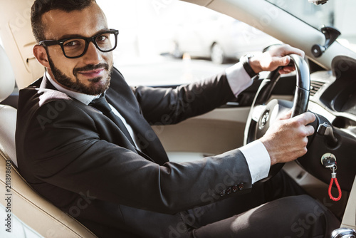 side view of handsome driver in suit driving car and looking at camera © LIGHTFIELD STUDIOS