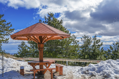 Wooden roof bench with snow on mountain view point with cloudy sky