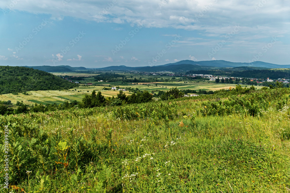 View from the hill to a small rural village in the background of green mountains and the endless blue sky