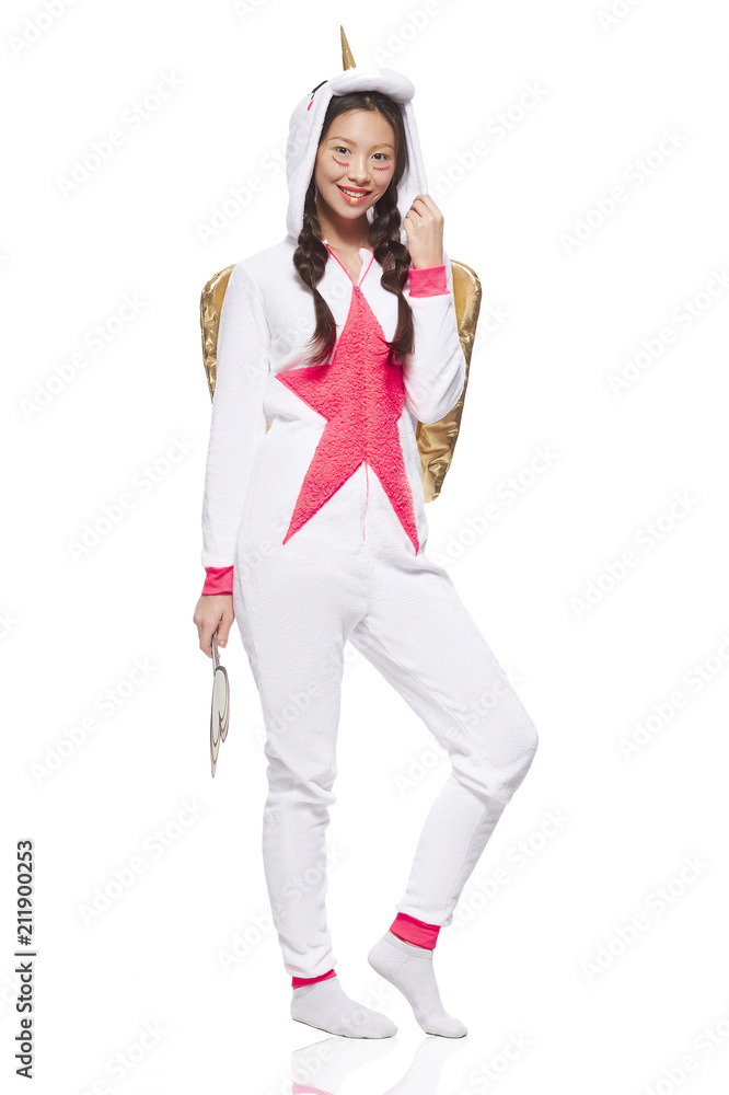 Fotka „A smiling Asian girl wearing a unicorn kigurumi costume, getting  ready for the cosplay or slumber party. The pajama-clad young lady looking  at the camera while posing against the white background. “