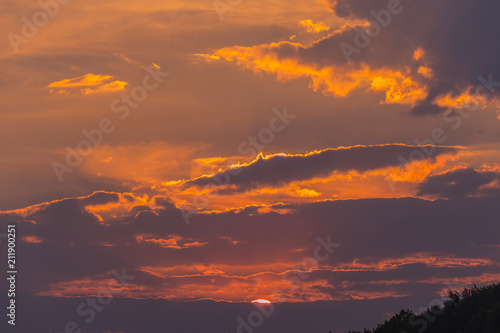 The beauty of the evening sky with clouds of red in the setting sun, a little more visible on the horizon © adamchuk_leo