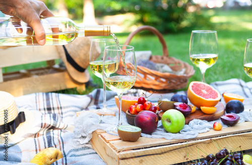 Picnic background with white wine and summer fruits on green grass, summertime party
