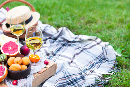 Picnic background with white wine and summer fruits on green grass, summertime party