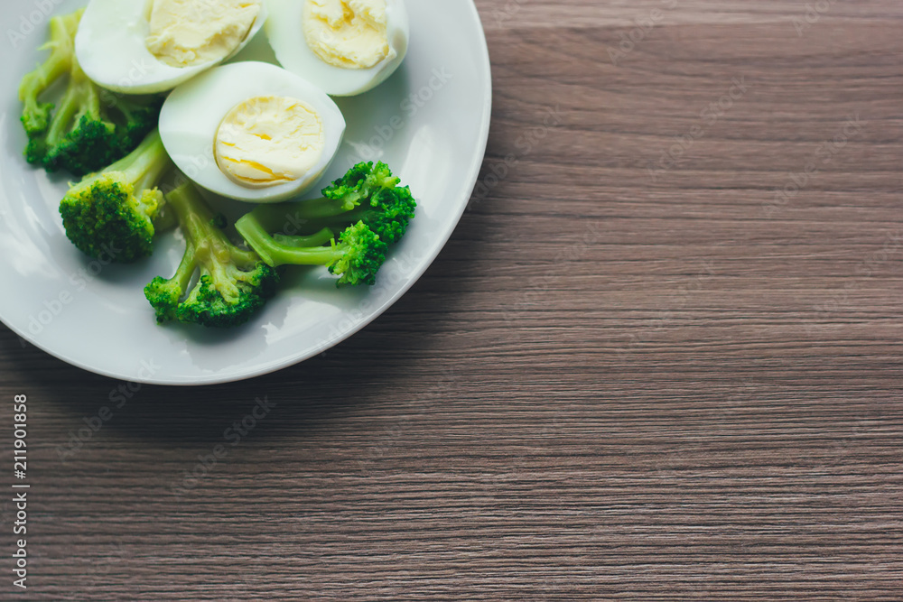 Boiled eggs and broccoli on a white plate on a wooden table.