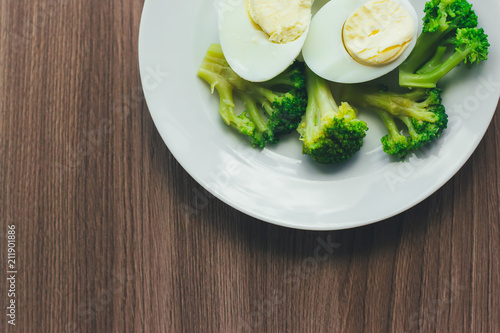 Boiled eggs and broccoli on a white plate on a wooden table.