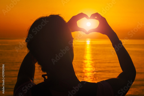 Silhouette of a girl at sunset with hands in the shape of a heart