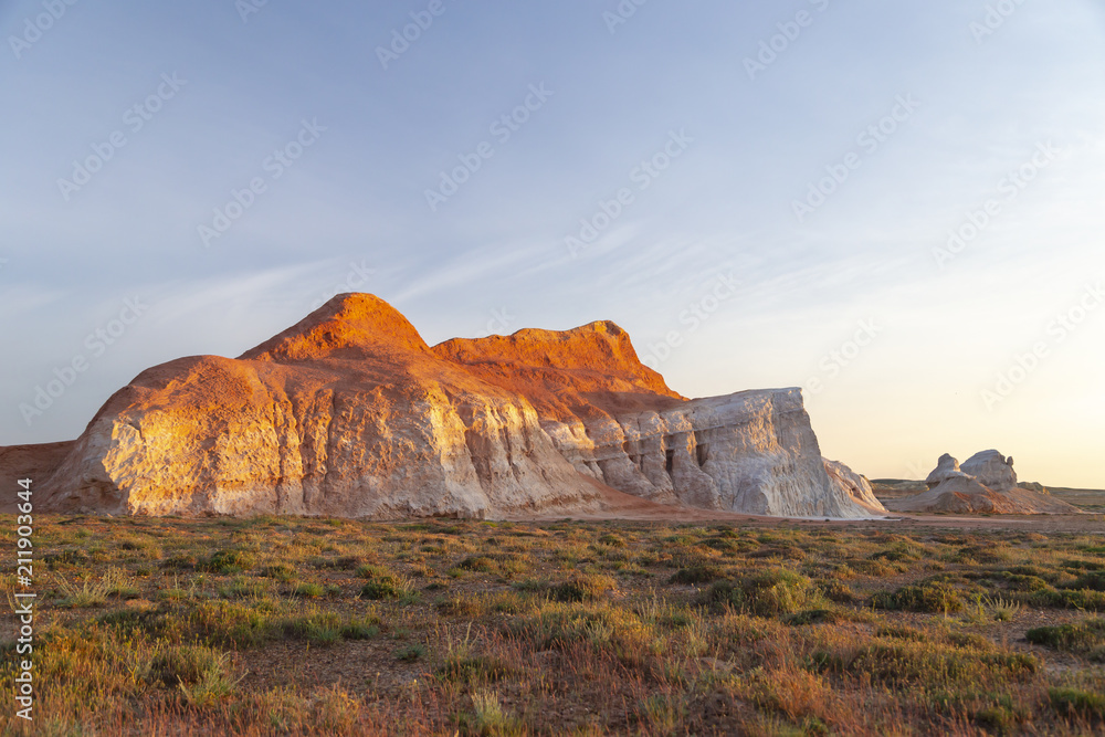 Multicolored red, orange and yellow single hill on the grass-covered steppe at sunset in Eastern Kazakhstan