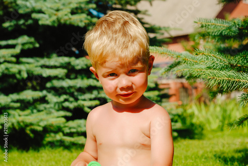 Closeup of little smiling interested cute male kid with blonde hair sitting outdoor lookling away on natural background