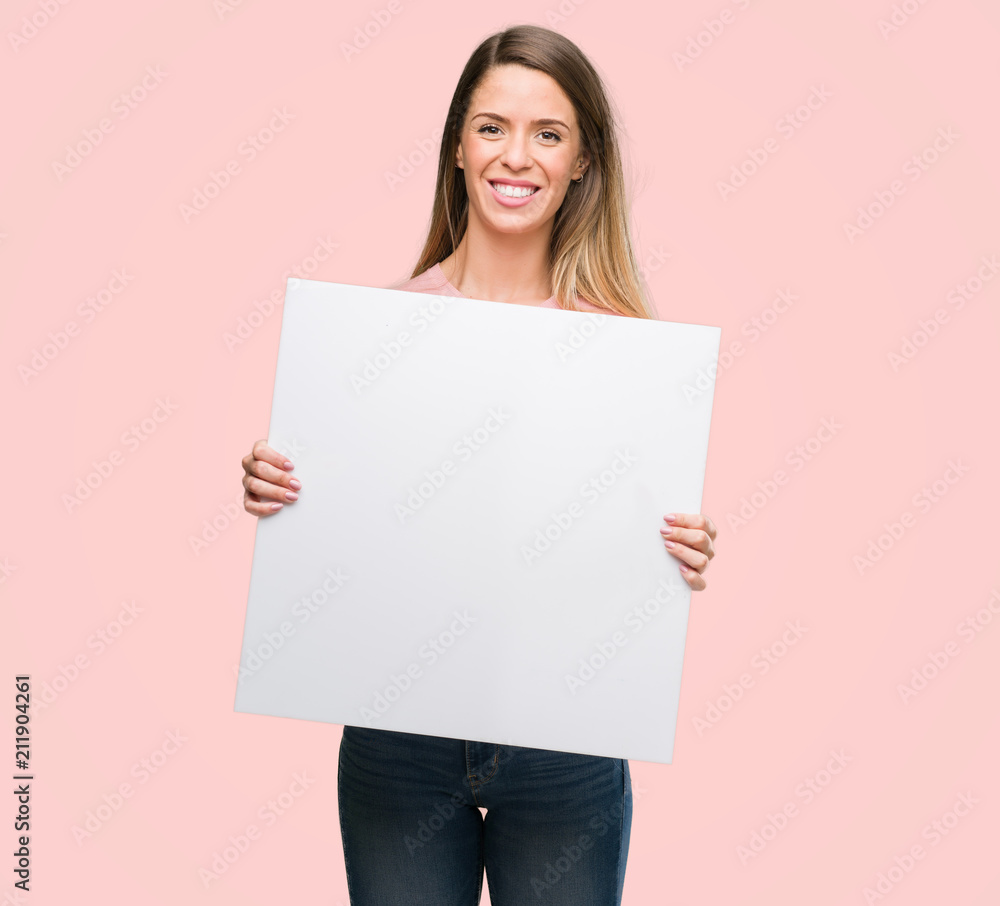 Beautiful young woman holding advertising banner with a happy face standing and smiling with a confident smile showing teeth Beautiful young woman holding advertising banner with a happy face standing and smiling with a confident smile showing teeth