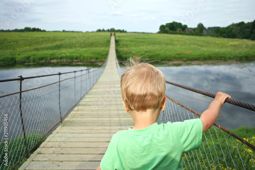 Cute toddler boy overcoming fear, prepering to crossing suspension bridge. Face your fears, look into the future, opening a new way concept photo