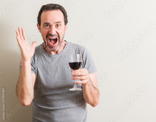 Senior man drinking red wine in a glass very happy and excited, winner expression celebrating victory screaming with big smile and raised hands
