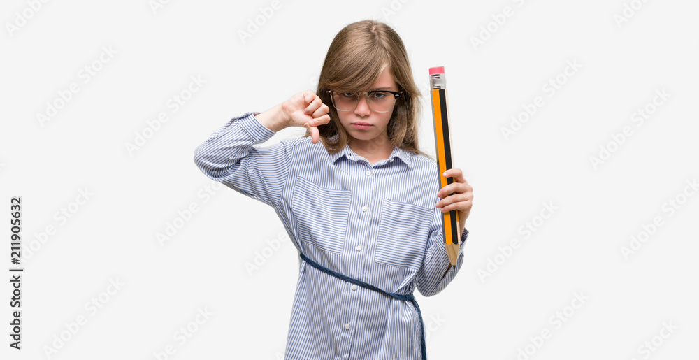 Young blonde child holding big pencil with angry face, negative sign showing dislike with thumbs down, rejection concept Young blonde child holding big pencil with angry face, negative sign showing dislike with thumbs down, rejection concept