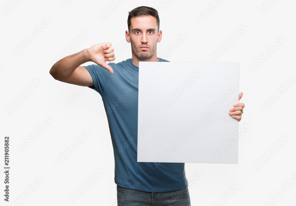 Handsome young man holding advertising banner with angry face, negative sign showing dislike with thumbs down, rejection concept Handsome young man holding advertising banner with angry face, negative sign showing dislike with thumbs down, rejection concept