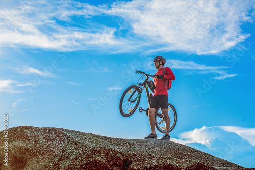 Fototapeta Naklejka Na Ścianę i Meble -  Cyclist man carrying his mountain bike along the rocky terrain on a sunny day against a blue sky