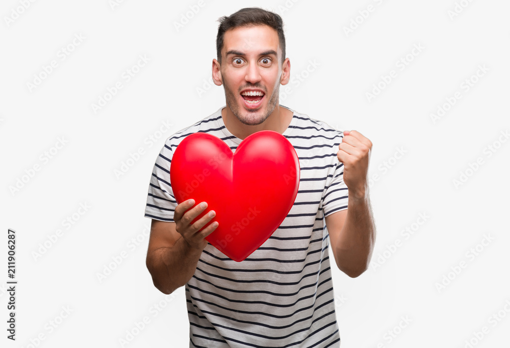 Handsome young man in love holding red heart screaming proud and celebrating victory and success very excited, cheering emotion Handsome young man in love holding red heart screaming proud and celebrating victory and success very excited, cheering emotion
