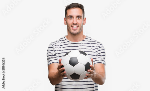 Handsome young man holding soccer football with a happy face standing and smiling with a confident smile showing teeth
