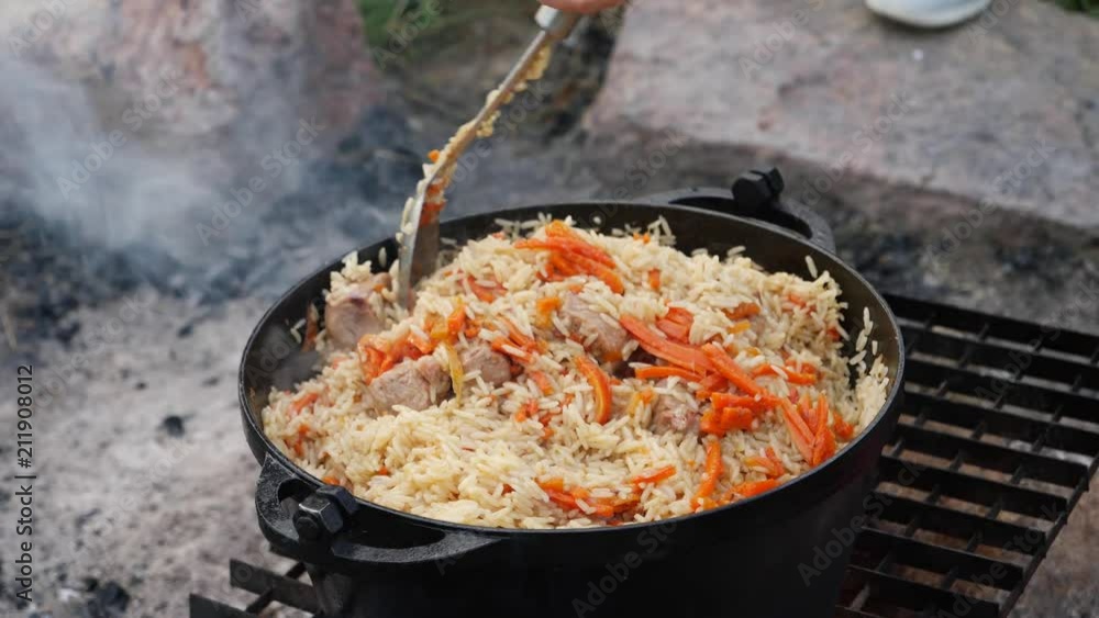 Cooking pilaf in a cauldron on the fire in camping - a dish with rice, meat and carrot Cooking pilaf in a cauldron on the fire in camping - a dish with rice, meat and carrot