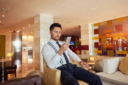 Handsome businessman looking for interesting multimedia applications in mobile phone store. Male gadget user downloading and updating new programs for his cellular telephone. photo