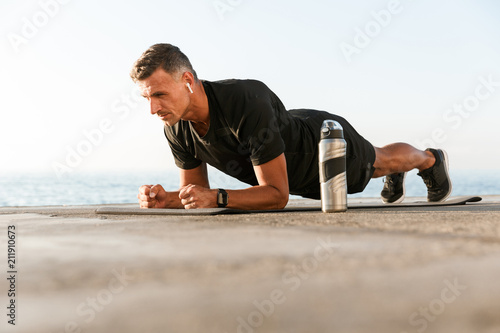 Confident sportsman in earphones doing plank