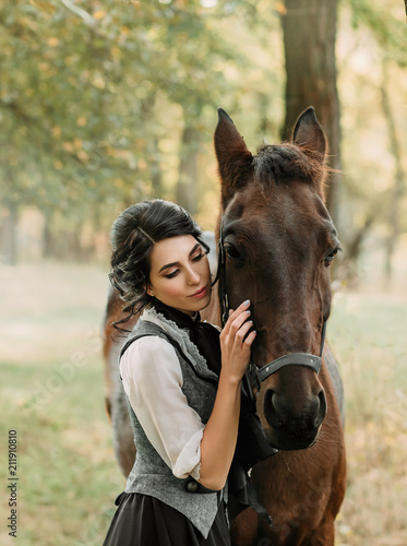 A young lady in a vintage dress, with tenderness and with affection hugs her horse. An ancient, collected hairstyle, a gentle make-up. Gold autumn background. Art photo © kharchenkoirina