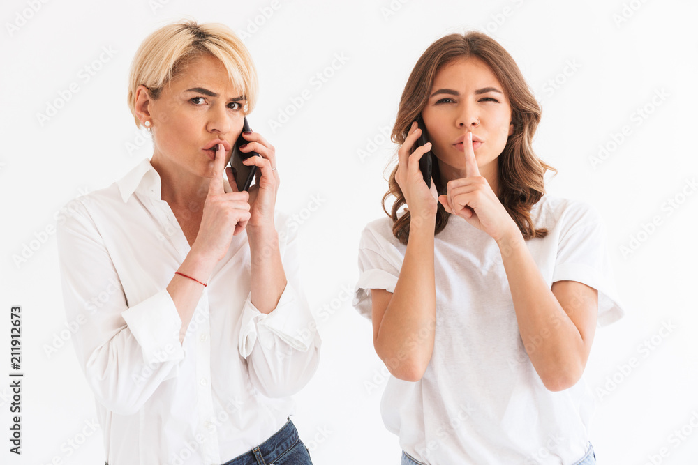 Woman standing with her mother talking by mobile phones Woman standing with her mother talking by mobile phones