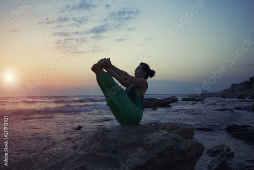 Girl is doing yoga standing in bridge pose setu bandhasana on rocks by the sea with sunse photo