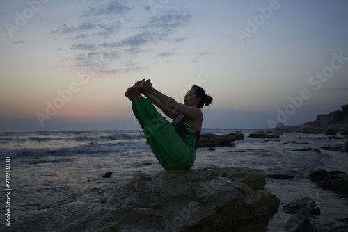 Girl is doing yoga standing in bridge pose setu bandhasana on rocks by the sea with sunse photo