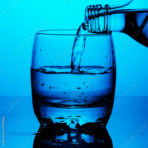 Clean drinking water is poured from a bottle a glass cup on blue background photo