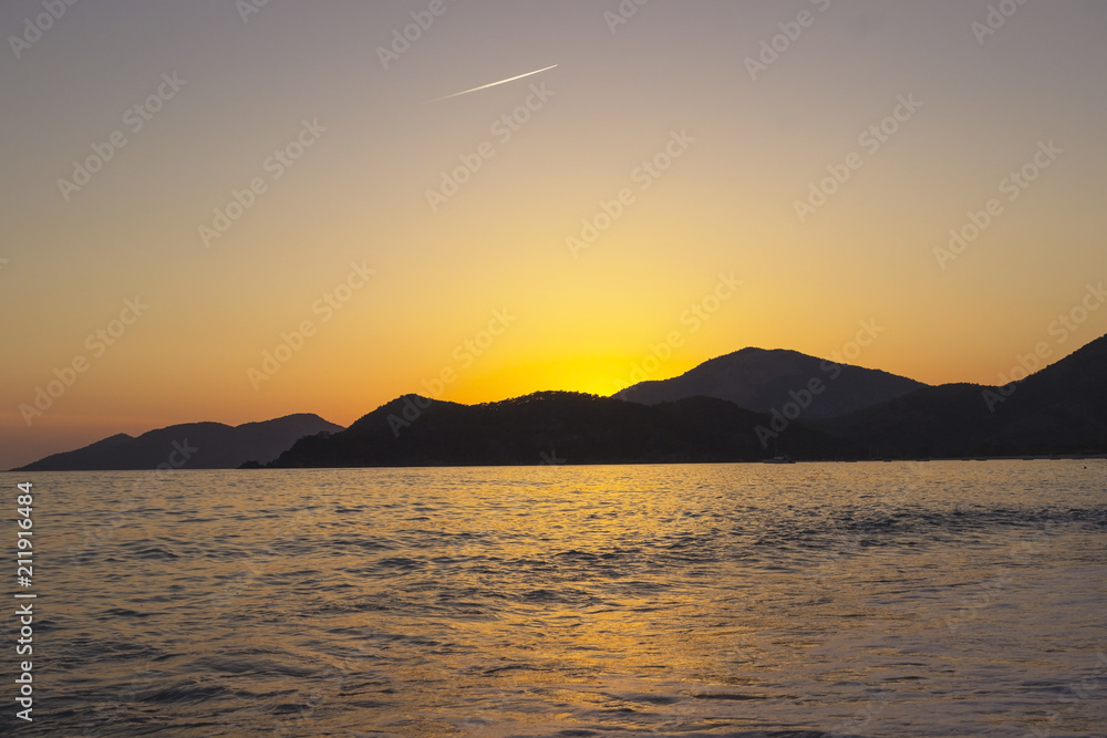 Mediterranean landscape. Sunset on the sea with flowing bright colored rays of the sun through the clouds. Silhouettes of mountains.  Background.
