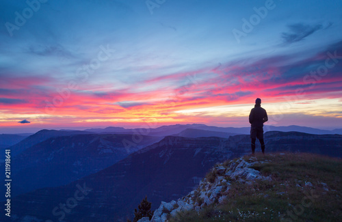 A hiker is looking at a pink sunset in a mountainous wilderness. © sanderstock