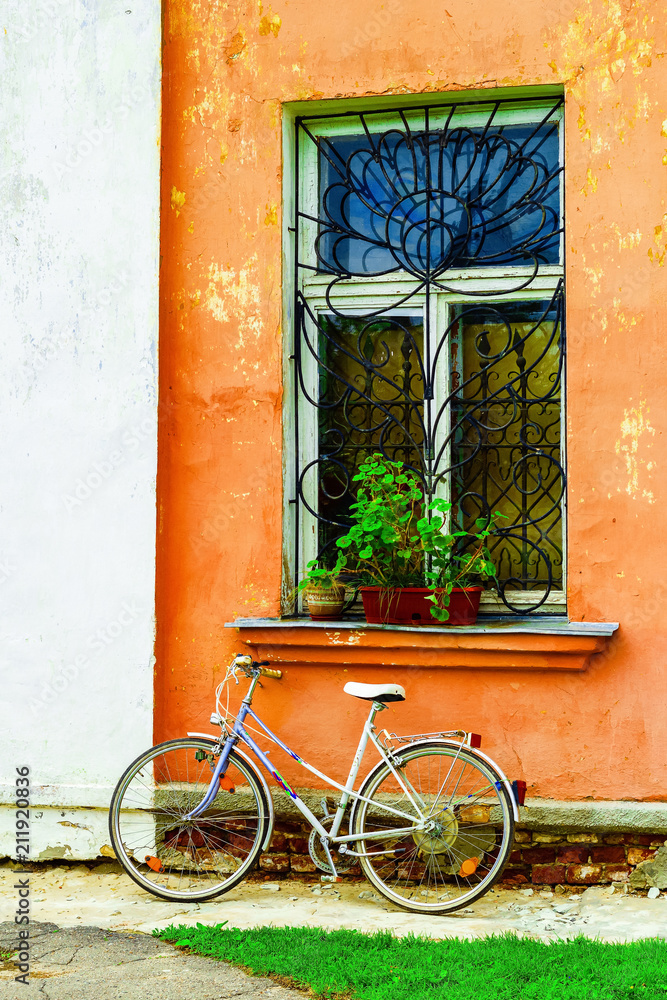 Old bicycle on a wall background with old, cracked plaster and a window with flowers.