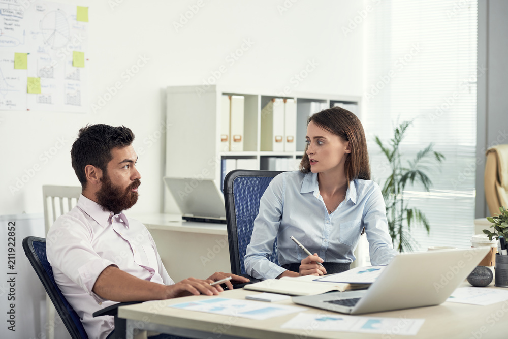 Professional young woman and man in formal clothes sitting at table in office working and speaking in team Professional young woman and man in formal clothes sitting at table in office working and speaking in team