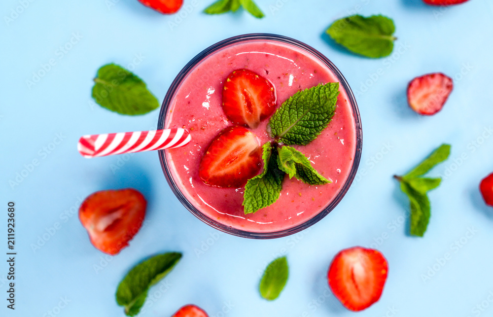 Naklejka premium A glass of strawberry smoothie with mint on a blue background. Nearby lie pieces of strawberries and mint leaves.