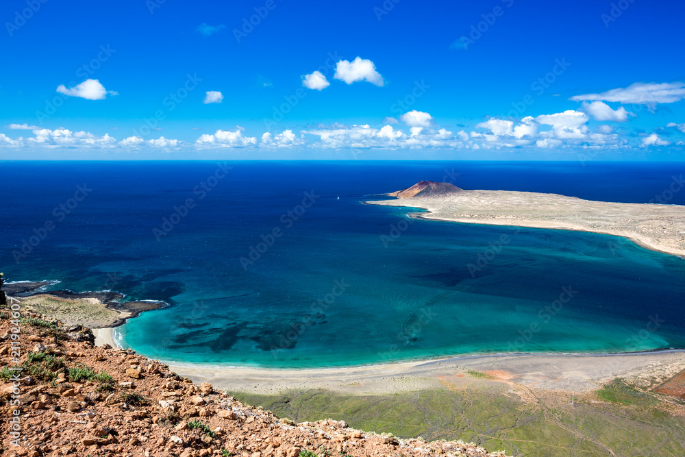 Lanzarote, Canary Islands, Spain, elevated landscape view of the blue Atlantic Ocean with a distant sleeping volcano on a nearby island. Blue sky with layered white clouds