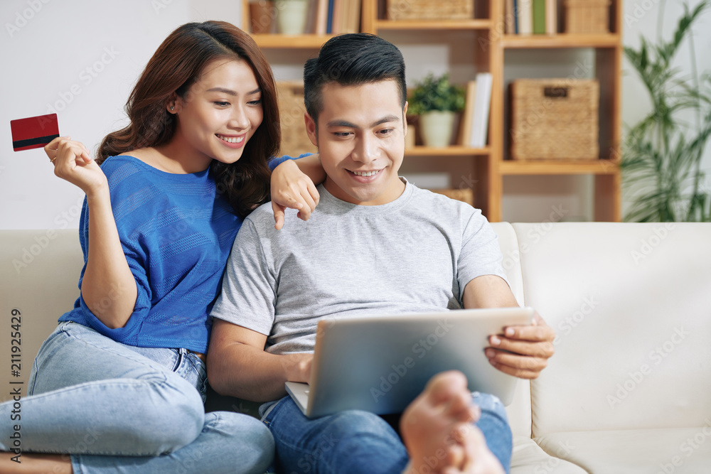 Beautiful Asian woman and man chilling on sofa with laptop and shopping in Internet with credit card Beautiful Asian woman and man chilling on sofa with laptop and shopping in Internet with credit card