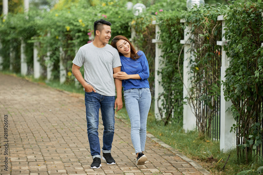 Loving young Asian couple holding hands and walking on pathway in summer green park being in love Loving young Asian couple holding hands and walking on pathway in summer green park being in love