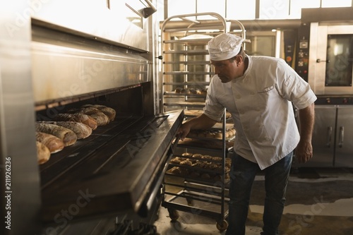 Male baker using baking owen in bakery shop photo