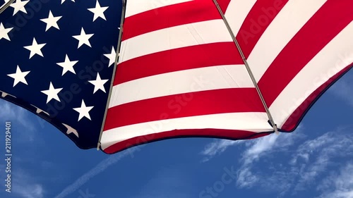 Stars and stripes American flag beach umbrella blowing in summer wind under bright blue sky