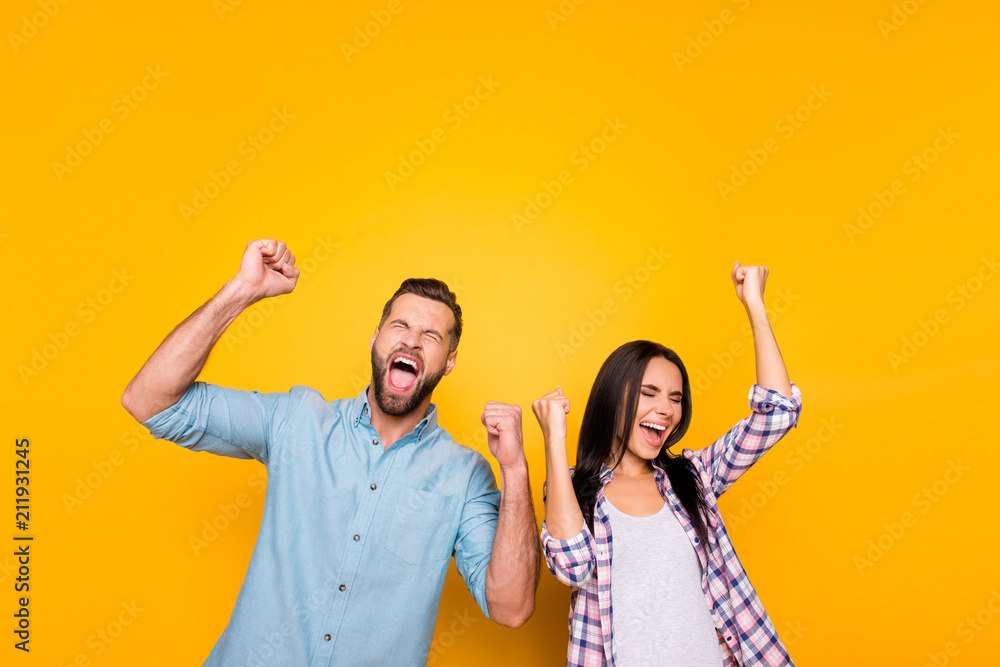 Portrait of crazy man couple full of happiness yelling loudly holding raised arms keeping eyes closed celebrating victory isolated on vivid yellow background - obrazy, fototapety, plakaty 