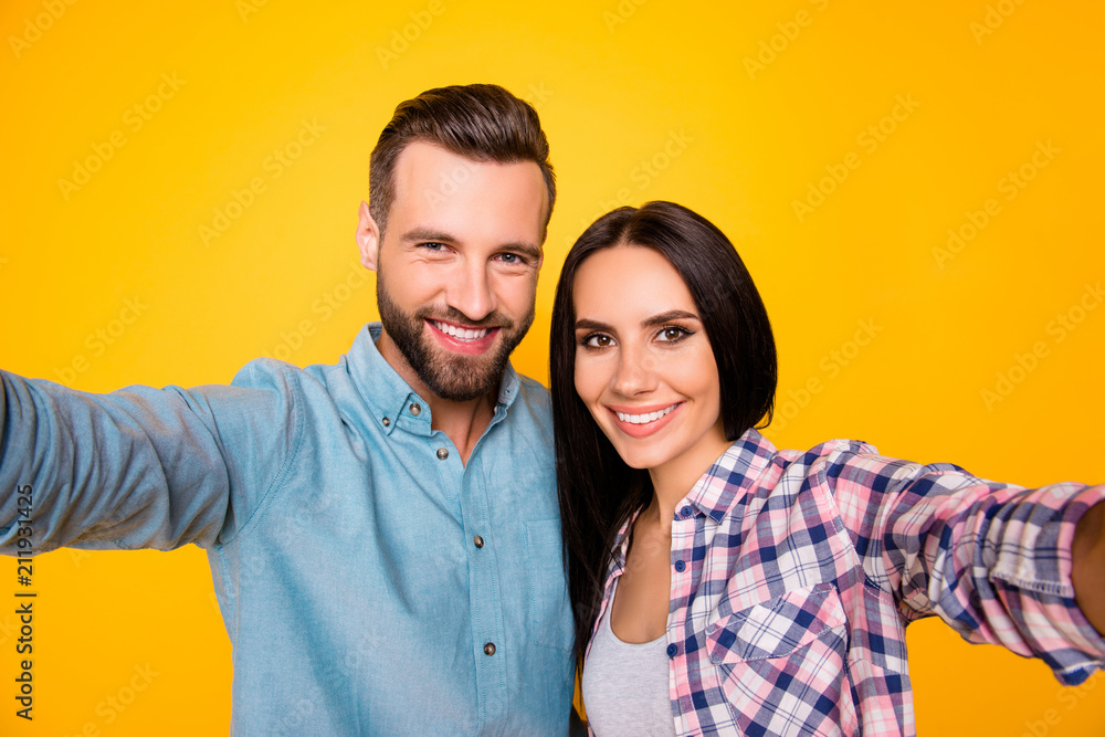 Self portrait of lovely attractive couple hugging shooting selfie on front camera having beaming smiles wearing casual shirts isolated on vivid yellow background Self portrait of lovely attractive couple hugging shooting selfie on front camera having beaming smiles wearing casual shirts isolated on vivid yellow background
