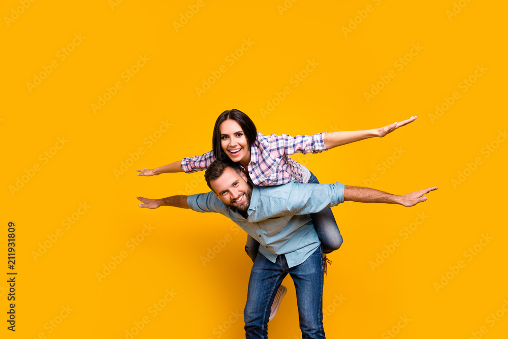 Obraz premium Low angle view portrait of playful foolish couple making air plane holding hands to the side looking at camera isolated on vivid yellow background