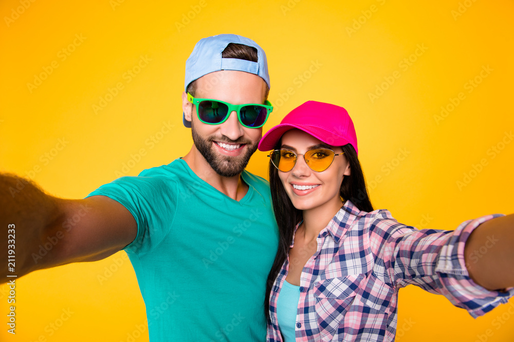 Self portrait of stylish trendy students in modern eyeglasses colorful headwear shooting selfie on front camera having beaming smiles isolated on bright yellow background Self portrait of stylish trendy students in modern eyeglasses colorful headwear shooting selfie on front camera having beaming smiles isolated on bright yellow background