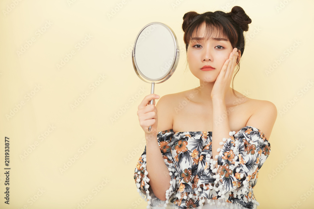 Portrait of attractive young woman looking at her face in the mirror Portrait of attractive young woman looking at her face in the mirror
